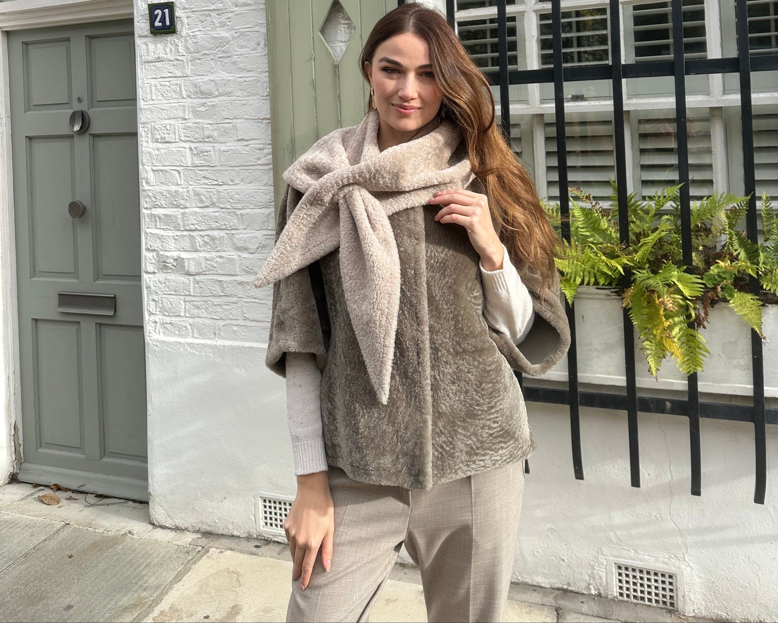Woman in a long coat standing in front of a building with a decorative metal gate.