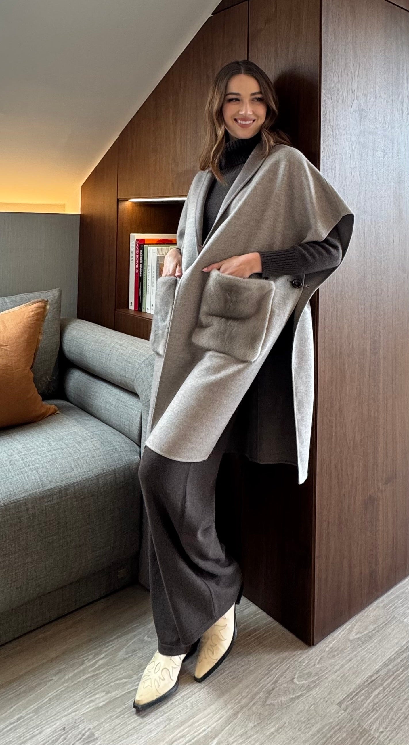 Woman standing in a modern living room wearing a gray poncho.