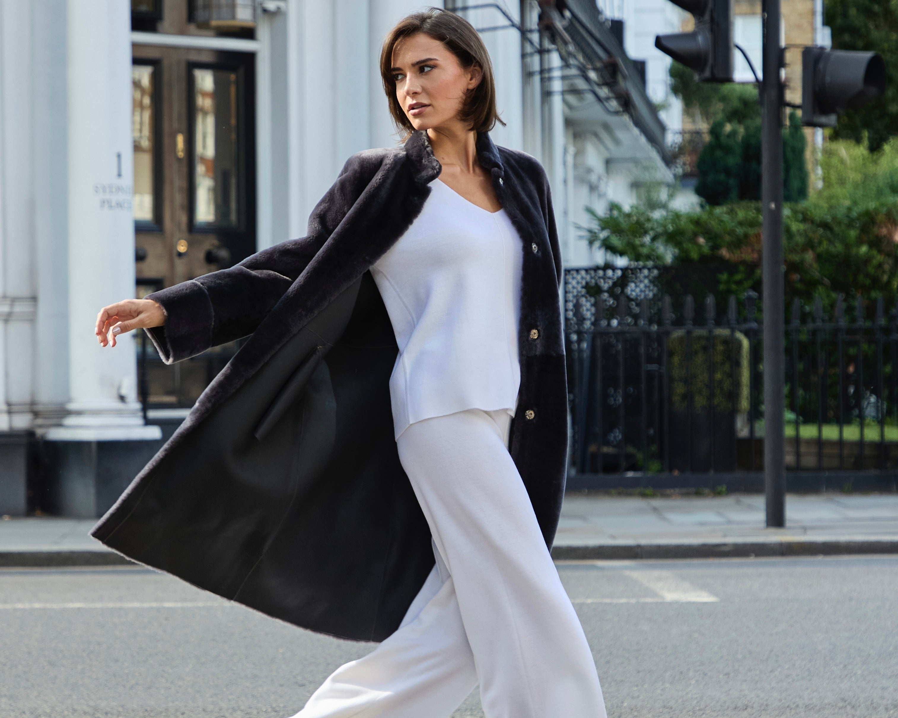 Woman in a black coat and white outfit crossing a street in an urban setting